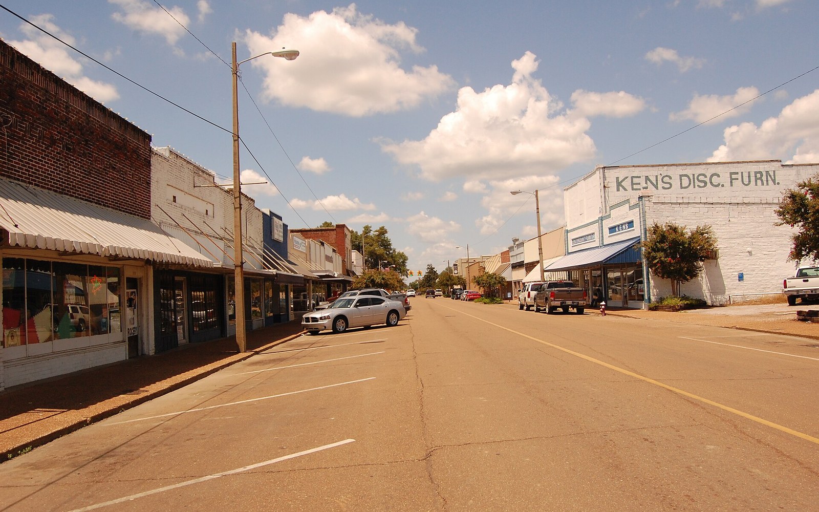 A quiet small-town main street lined with brick storefronts including Ken's Discount Furniture