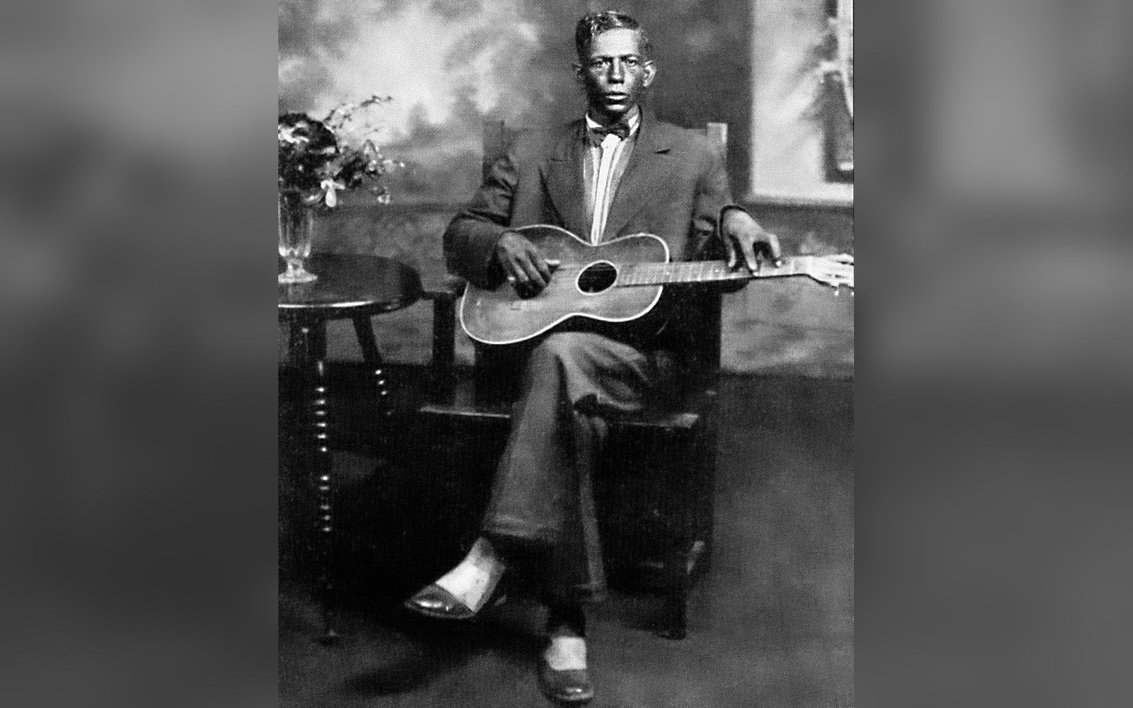 Vintage studio portrait of a seated man in a suit holding an acoustic guitar