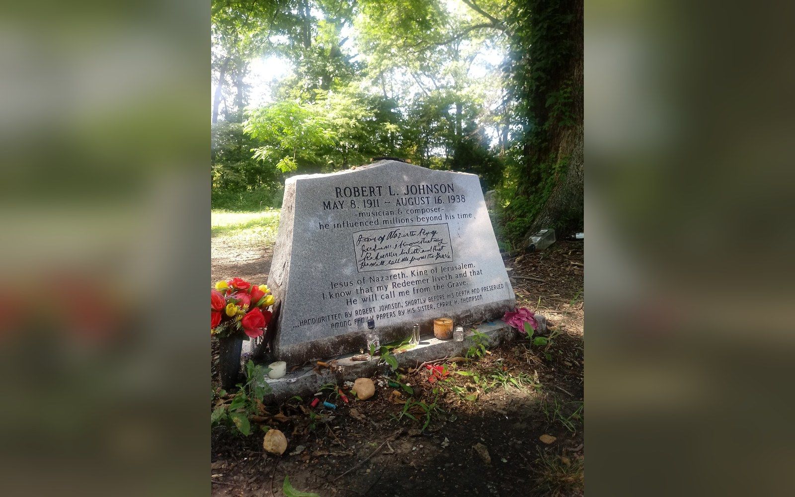 Robert L Johnson's gravestone surrounded by trees, with flowers and mementos left at its base