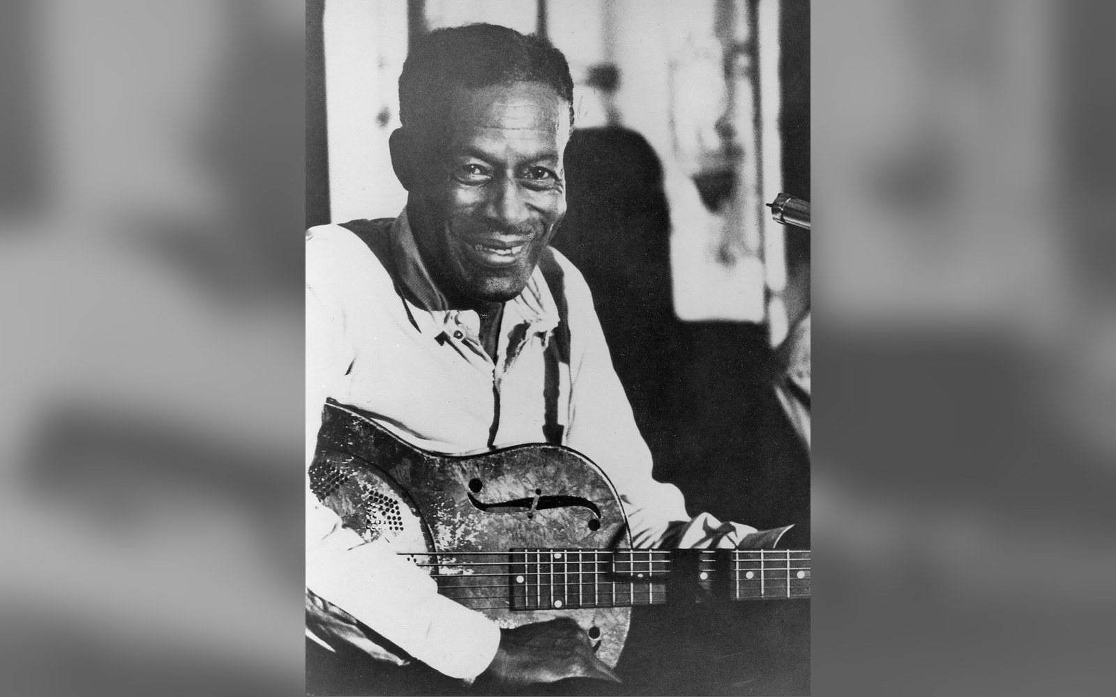 Black and white portrait of a smiling man holding a resonator guitar