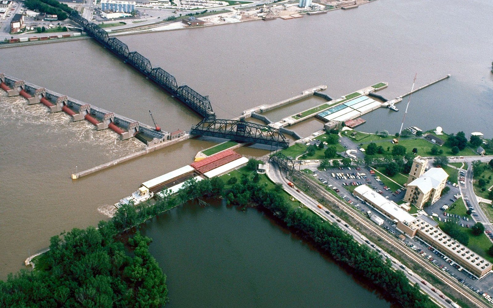 Aerial view of a river dam, swing bridge, locks, and adjacent riverside town