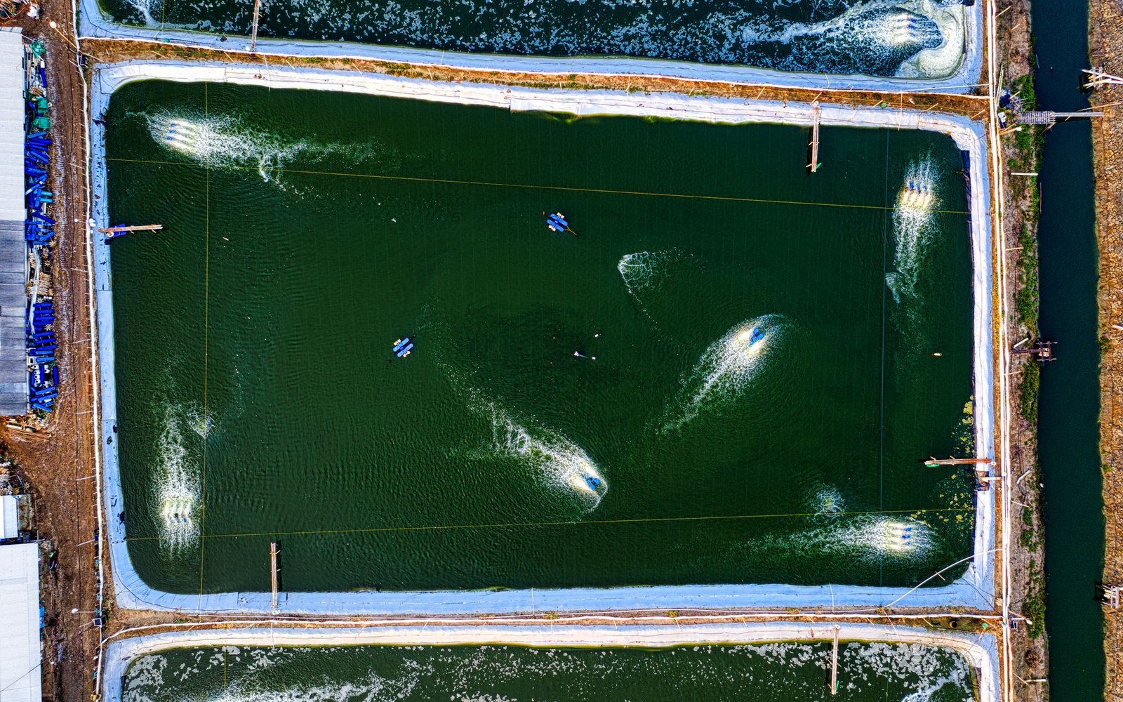 Aerial view of aerators churning water in a rectangular fish farming pond