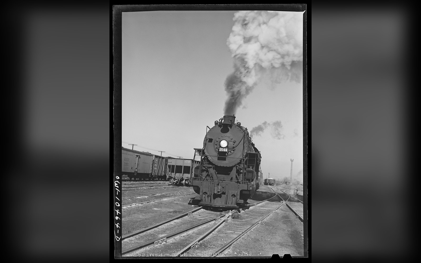 Steam locomotive billowing smoke as it approaches on rail yard tracks